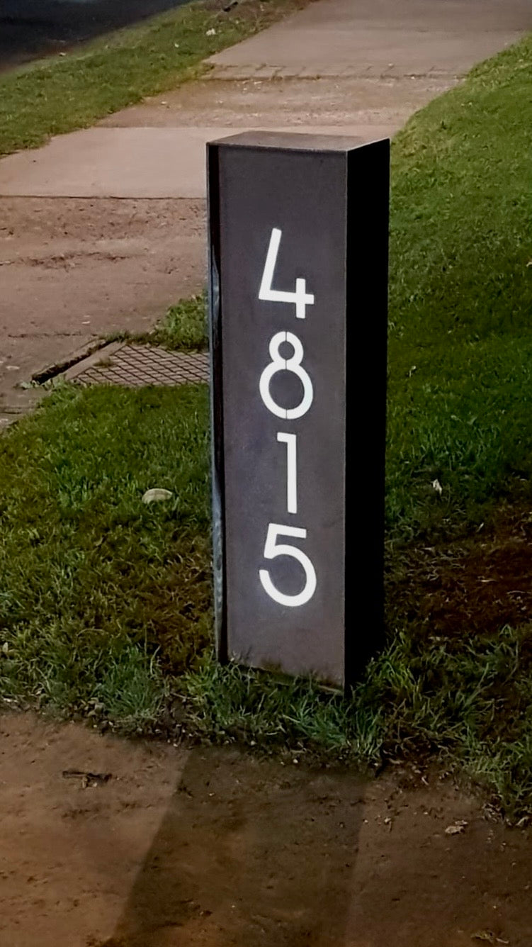 Foto de cliente, testimonio compra, efecto contraste con blanco. Estructura de metal tipo tótem, fabricado por capas, soldadura calidad, número de edificio, diseño personalizado, acero metal limpio, letrero domicilio, números de acero, plasma CNC fabricado en Chile, numeración vertical, diseño chileno, tipografía original, Santiago, Chile, región de Metropolitana, anclaje incluido, envío a domicilio. Acero natural, diseño único y original de IronPig. Letrero retroiluminado