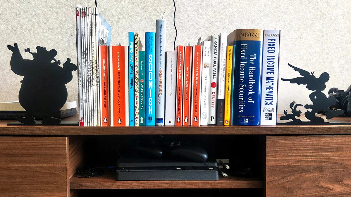 Sujeta libros decorativos de acero negro con siluetas de Obélix y Astérix, flanqueando colección de libros en estantería de madera, fabricados a medida por IronPig Chile