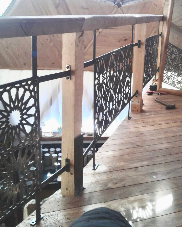 Baranda de acero calado con diseño geométrico de estrella instalada en pasillo interior de domo geodésico con piso y estructura de madera, testimonio real fabricada a medida por IronPig Chile