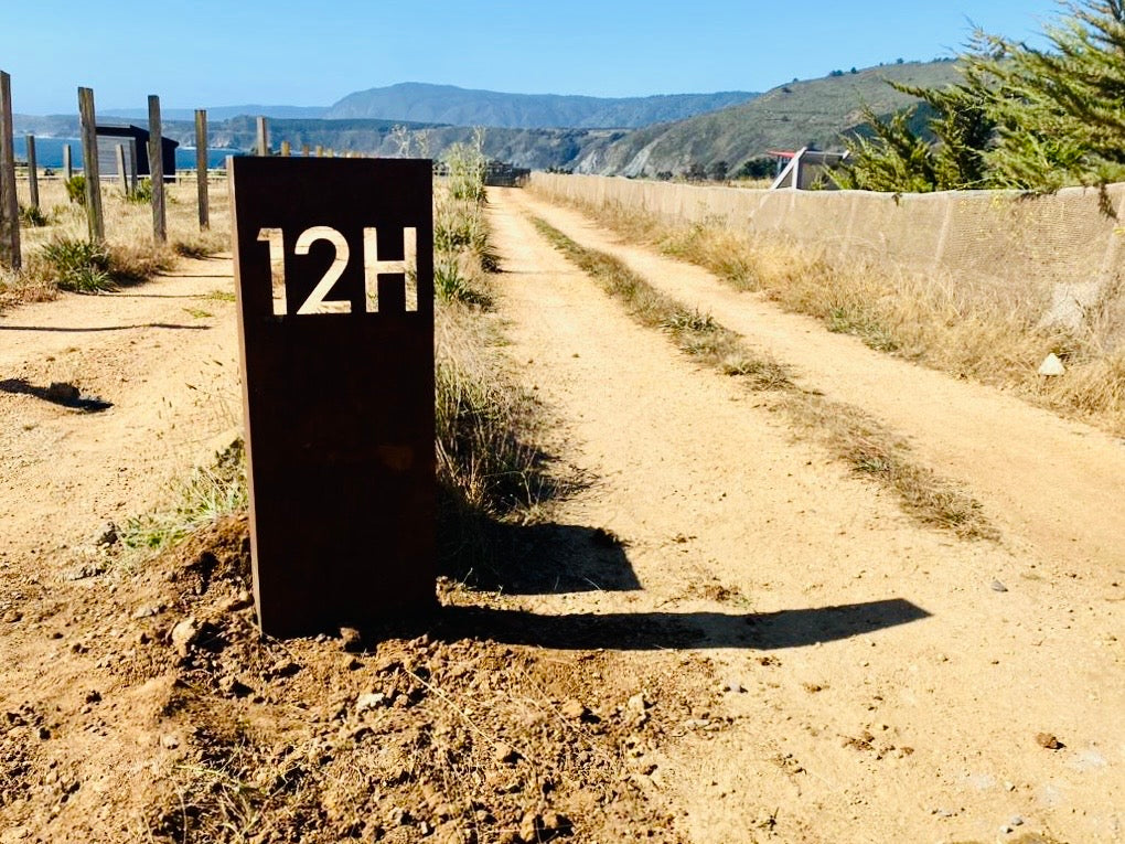 Foto de cliente, testimonio compra, diseño de letrero con número de parcela, hecho en metal. Estructura de metal tipo tótem, soldadura de calidad, número de casa, diseño personalizado, acero oxidado, letrero domicilio, números de acero, plasma CNC, fabricado en Chile, numeración horizontal, diseño chileno, domicilio en la playa, tunquen, Chile, región de Valparaíso, anclaje incluido, envío a domicilio. Acero natural, diseño único y original de IronPig. 