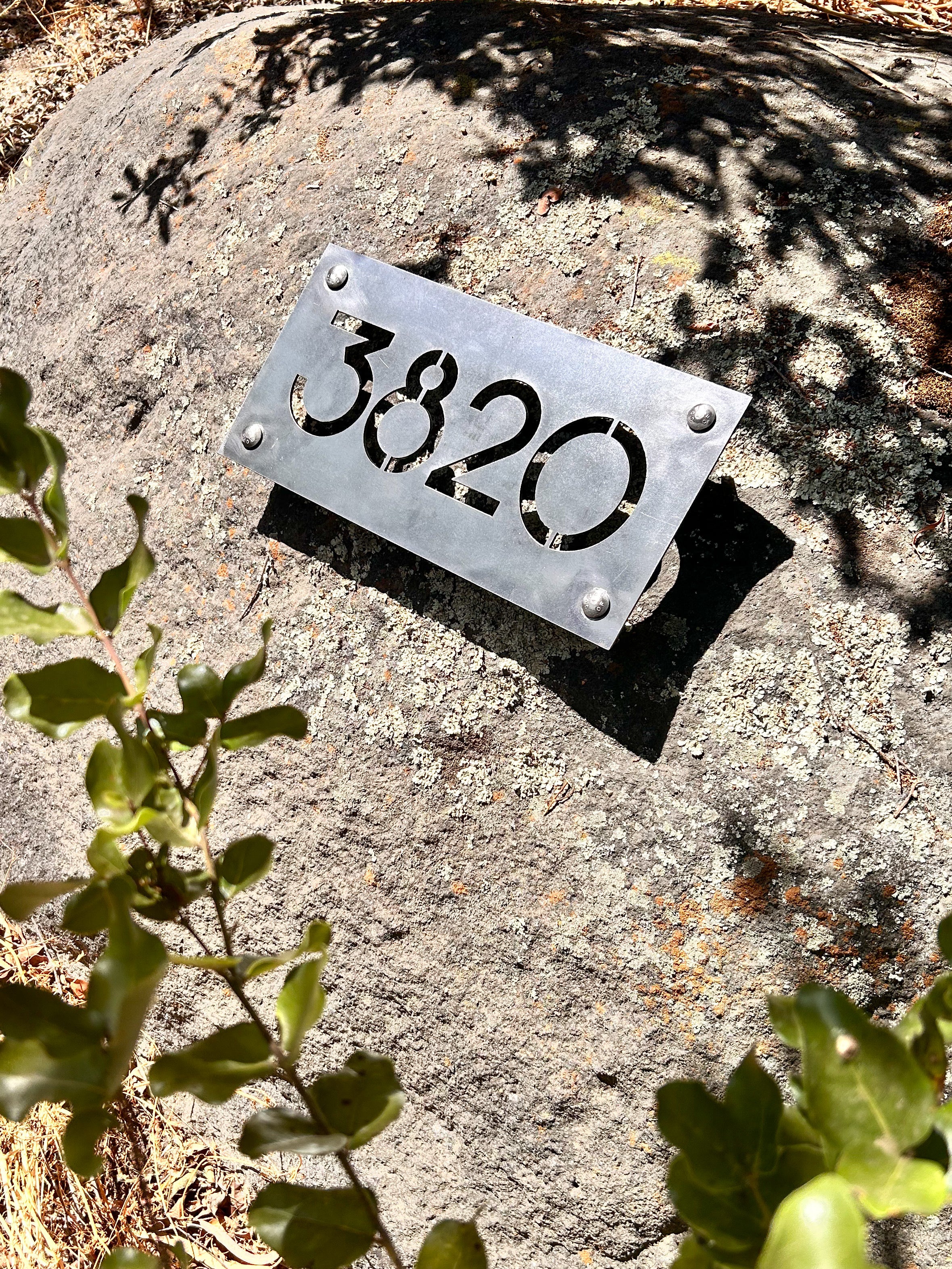 Placa de acero resistente a la intemperie, con número residencial calado. Diseño personalizado de número para casa. Detalle de cabezas de pernos asomadas por el frente. 