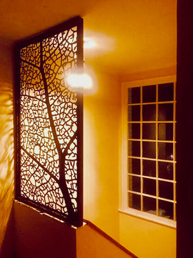 Panel decorativo de acero calado con diseño orgánico de nervaduras de hoja, instalado en escalera hacia segundo piso, acero con acabado oxidado encerado, diseño personalizado, fabricado a medida por IronPig Chile, testimonio real cliente