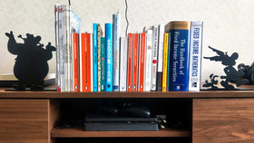 Sujeta libros decorativos de acero negro con siluetas de Obélix y Astérix, flanqueando colección de libros en estantería de madera, fabricados a medida por IronPig Chile
