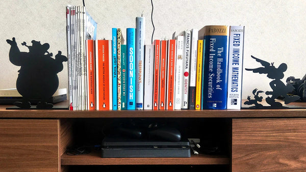 Sujeta libros decorativos de acero negro con siluetas de Obélix y Astérix, flanqueando colección de libros en estantería de madera, fabricados a medida por IronPig Chile
