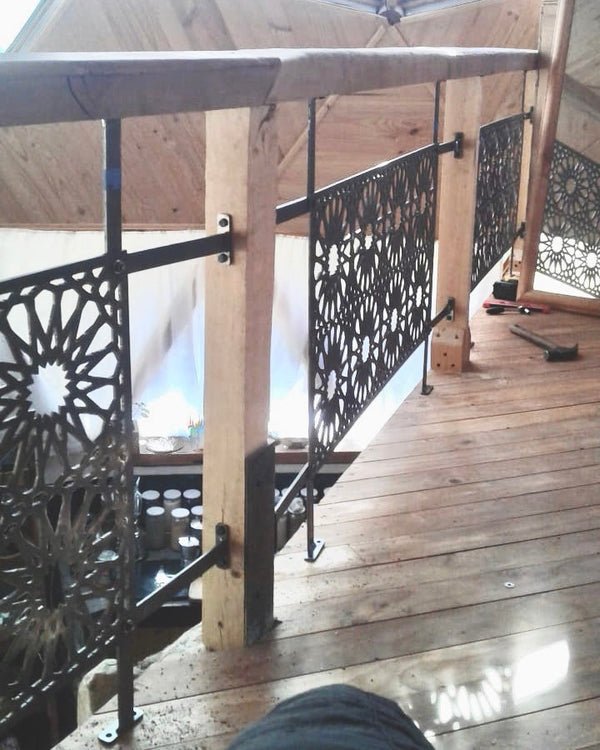 Baranda de acero calado con diseño geométrico de estrella instalada en pasillo interior de domo geodésico con piso y estructura de madera, testimonio real fabricada a medida por IronPig Chile
