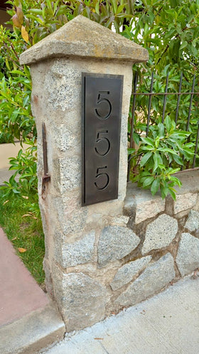 Placa de acero natural con número de casa personalizada, diseño calado en vertical, instalada en pilar de piedra natural en acceso residencial, fabricada a medida por IronPig Chile, testimonio cliente, envió a regiones
