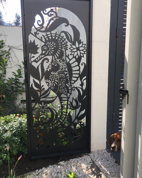Reja de acero calado con diseño artístico de caballito de mar y flores instalada en acceso exterior de jardín, fabricada a medida por IronPig Chile
