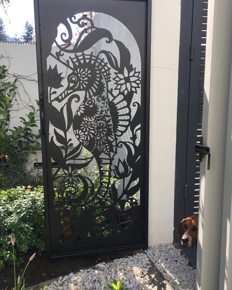 Reja de acero calado con diseño artístico de caballito de mar y flores instalada en acceso exterior de jardín, fabricada a medida por IronPig Chile
