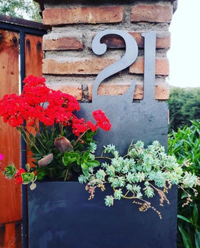Número de casa en acero decorativol, instalado sobre muro de ladrillos, diseño de número domicilio con macetero ideal para plantas, suculentas y flores rojas, casa entrada alegre natural acogedora, fabricado por IronPig Chile. Testimonio cliente