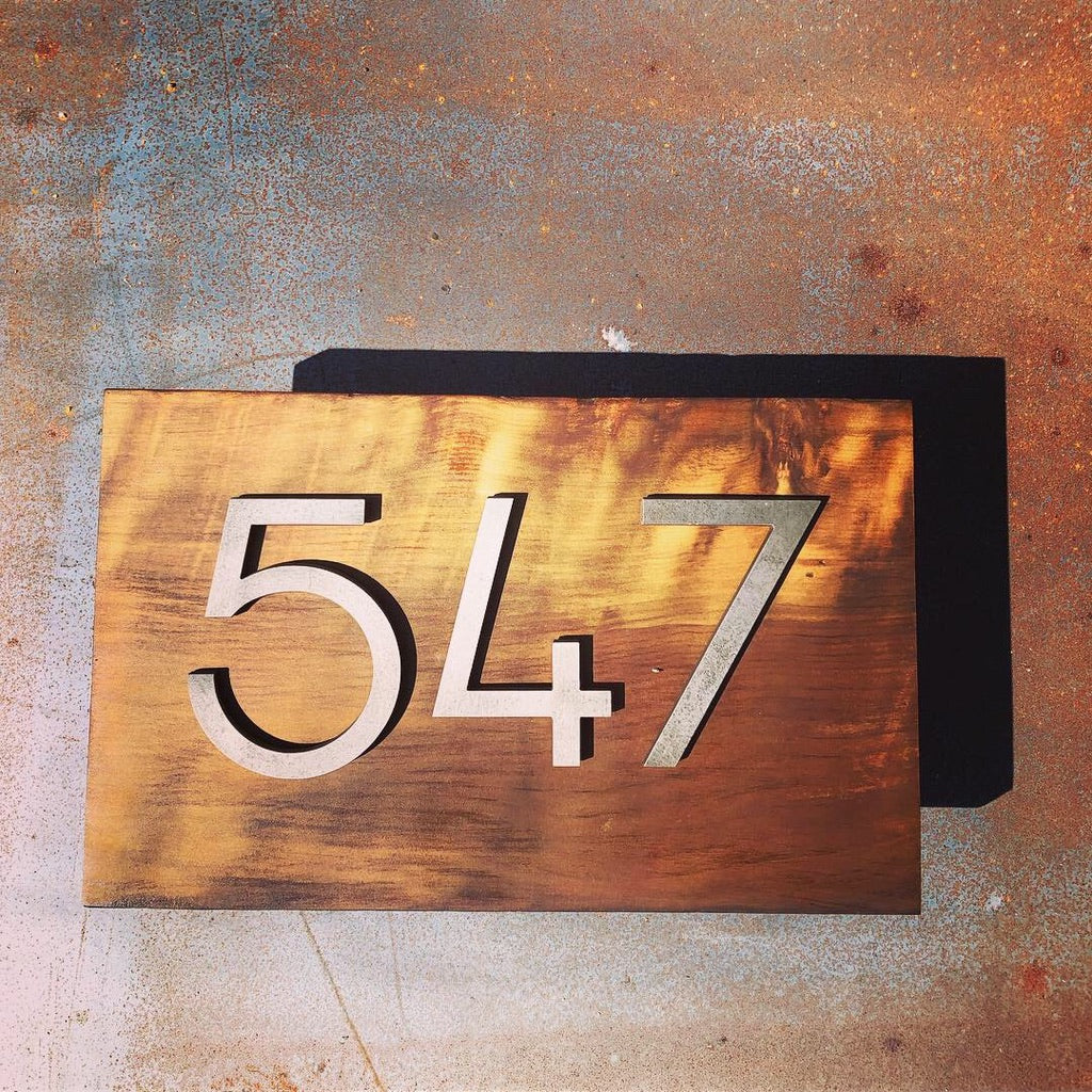 Número sobre placa de madera con cifras en acero negro para fachada